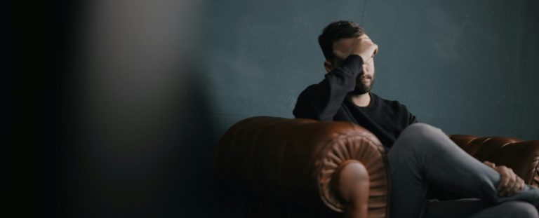 man holding his forehead in anxiety siting on the couch