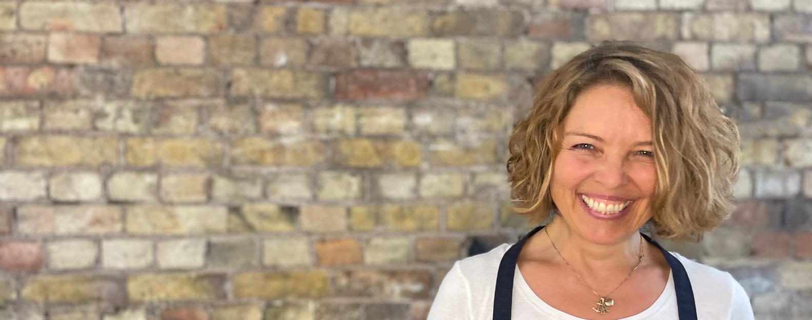 Anu Paavola, smiling against a brick wall