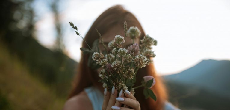 Woman hiding behind bunch of picked flowers in front of her face.